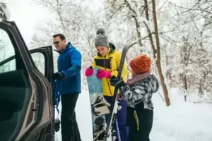 Smiling family holding skis while stopping on a winter road trip in the mountains