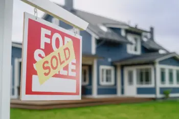 Close Up of a House Sold Sign on a Lawn in Front of a Big Modern House with Traditional Architecture