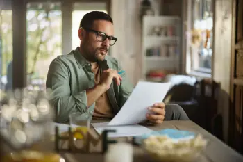 Mid adult man brainstorming while examining insurance paperwork at home